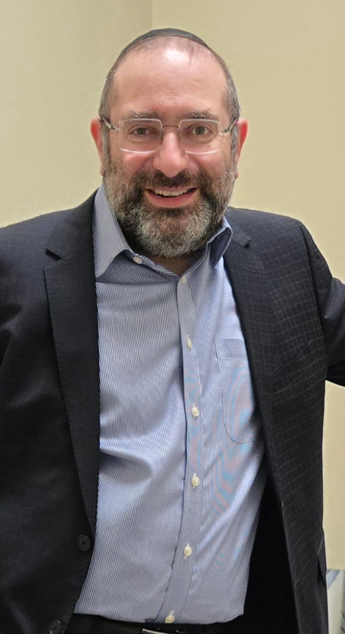Portrait of Dr. Shimon Blau, smiling, wearing glasses and a navy blazer over a light blue shirt.